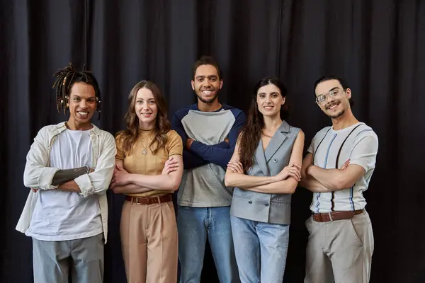 Group photo of happy and stylish multiethnic team with folded arms near black drape in office — Stock Photo