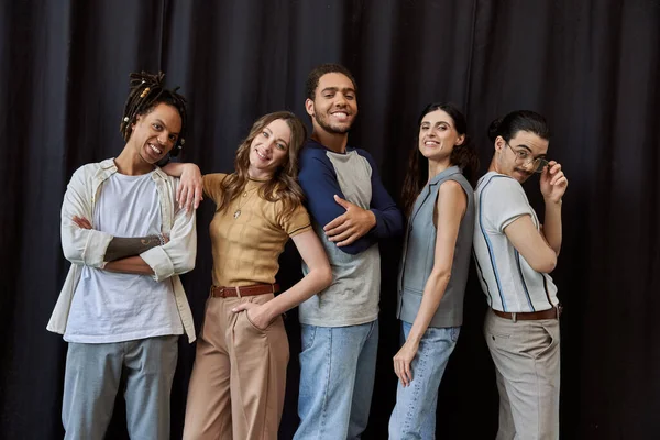 Joyful multiethnic colleagues in casual attire looking at camera near black drape in modern office — Stock Photo