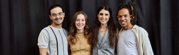 Веселая многонациональная команда стартапов в повседневной одежде, стоящая возле черной занавески в офисе, баннер — стоковое фото