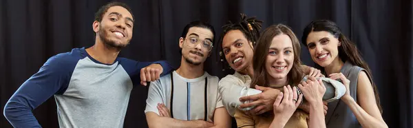 Foto da equipe multiétnica feliz abraçando e olhando para a câmera no fundo preto no escritório, banner — Fotografia de Stock
