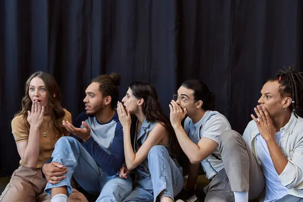 Multiethnic colleagues sitting and telling gossip to shocked woman near black drape in office — Stock Photo