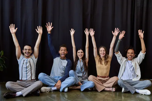 Emocionado equipo multiétnico elegante sentado y agitando las manos cerca de drapeado negro en la oficina, foto de grupo - foto de stock