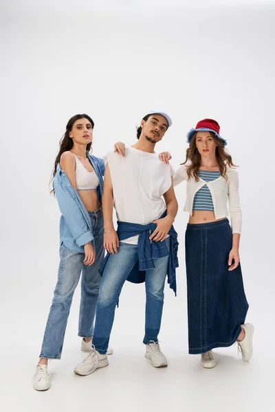 Full length of confident friends in trendy clothes and jeans wear looking at camera on grey backdrop — Stock Photo