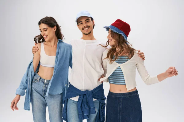 Joyeuse jeune femme embrassant femme en tenue décontractée à la mode et regardant la caméra sur fond gris — Photo de stock