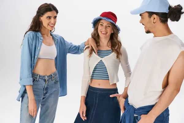 Donna allegra in abiti di denim sorridente vicino amici alla moda su sfondo grigio, moda moderna — Foto stock