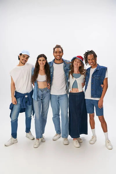 Longitud completa de amigos multiculturales en ropa de calle casual con estilo sonriendo a la cámara en el fondo gris - foto de stock