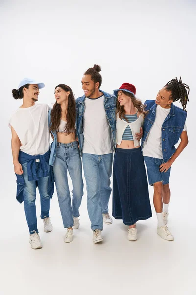 Diverse group of smiling multiethnic friends in stylish casual attire embracing and walking on grey — Stock Photo