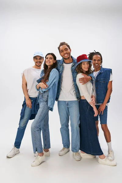 Homme afro-américain joyeux embrassant amis interracial à la mode regardant caméra sur gris — Photo de stock