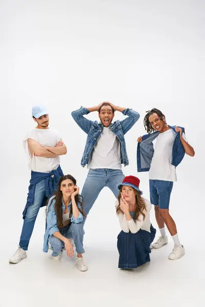 Excited multicultural men posing near stylish women squatting on grey backdrop, street style — Stock Photo