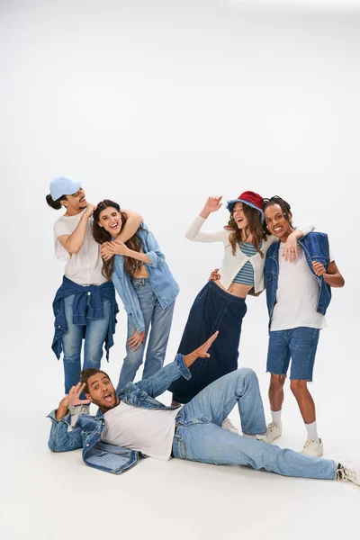 Excited african american man lying down near happy interracial friends embracing on grey backdrop — Stock Photo