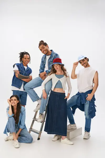 Lächelnde multiethnische Freunde in stylischer Streetwear posieren mit Leiter und blicken in die Kamera auf grau — Stockfoto