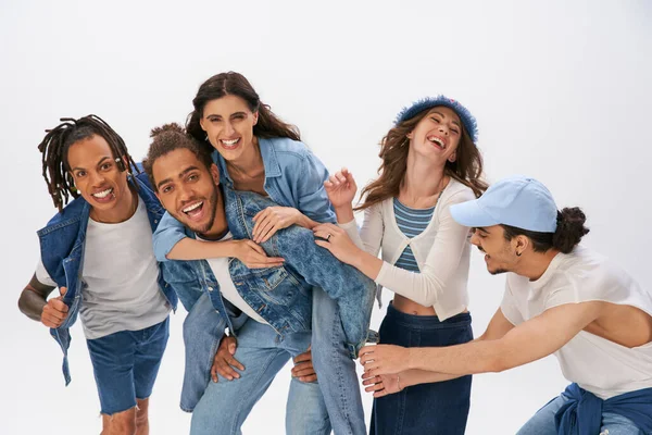 Happy african american man piggybacking woman near stylish interracial friends having fun on grey — Stock Photo