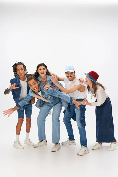 Excited african american man piggybacking woman near trendy interracial friends having fun on grey — Stock Photo