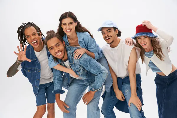 Trendy african american man piggybacking woman near excited multiethnic friends having fun on grey — Stock Photo