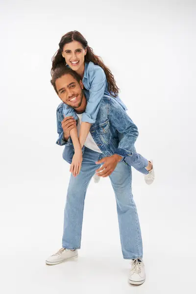 Homem americano africano elegante piggybacking namorada feliz em roupas jeans em cinza, comprimento total — Fotografia de Stock