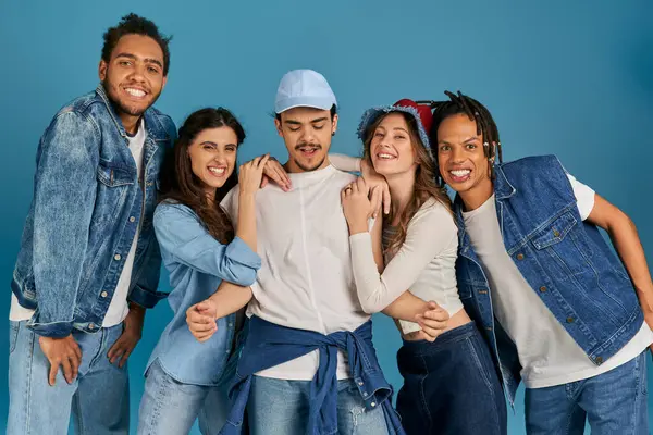 Cheerful and trendy multicultural friends posing near young man in cap on blue, modern fashion — Stock Photo