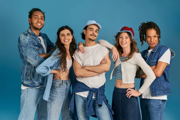 Amigos multiculturales felices en atuendo casual mirando a la cámara en azul, diversidad y moda - foto de stock