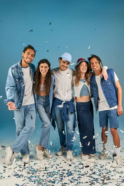 Fröhliche multiethnische Freunde in stylischer Streetwear lächeln unter festlichem Konfettiregen auf Blau — Stockfoto