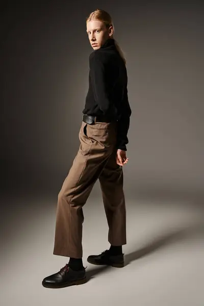 Young attractive non binary person with ponytail in black turtleneck posing with arms behind back — Stock Photo