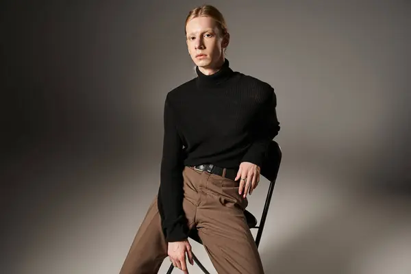 Attractive non binary model in black turtleneck with ponytail sitting on black chair, fashion — Stock Photo