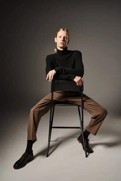 Vertical shot of young non binary person with red hair and ponytail sitting on black chair — Stock Photo