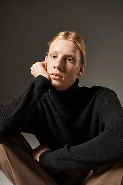 Vertical shot of young non binary model sitting on floor with crossed legs and looking at camera — Stock Photo