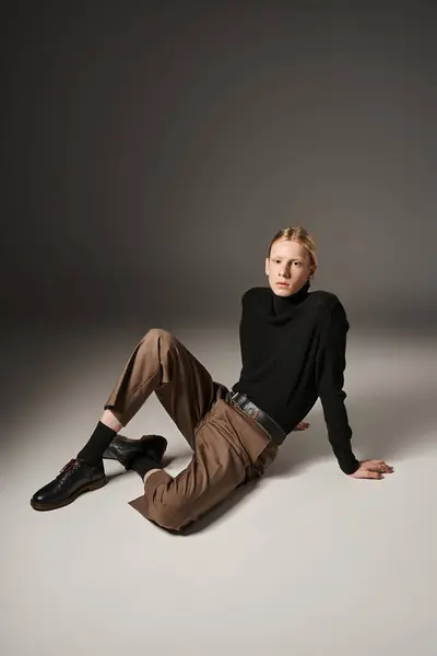 Attractive young non binary model with ponytail posing on floor and looking at camera, fashion — Stock Photo