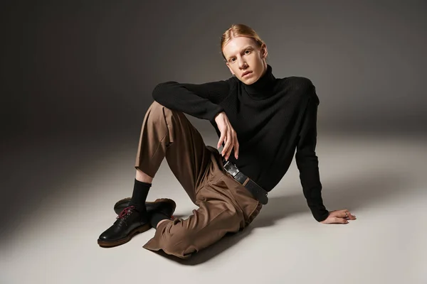 Young non binary person in black turtleneck sitting on floor and looking at camera, fashion concept — Stock Photo