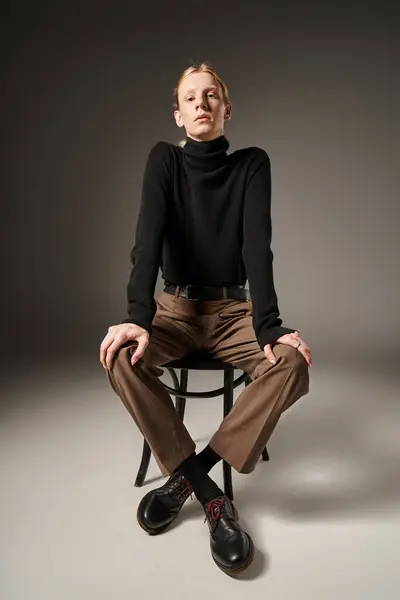 Tiro vertical de jovem não binário pessoa em gola alta preta sentado na cadeira e olhando para a câmera — Fotografia de Stock