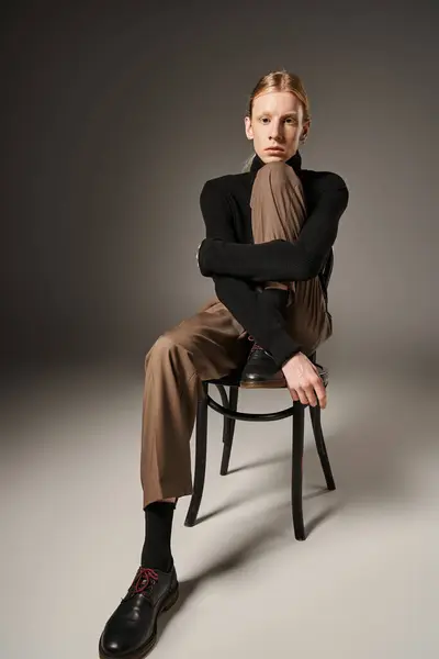 Jeune beau non binaire à col roulé assis sur la chaise et regardant la caméra, la mode — Photo de stock