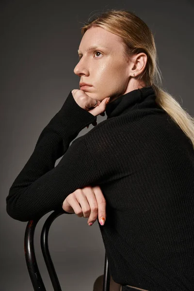 Junges nicht binäres Model in stylischer Kleidung posiert im Profil mit der Hand unter dem Kinn, sitzend auf Stuhl — Stockfoto