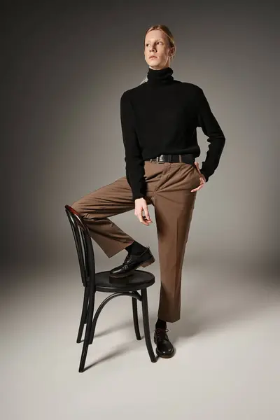 Vertical shot of attractive young non binary person posing with leg on black chair, fashion — Stock Photo