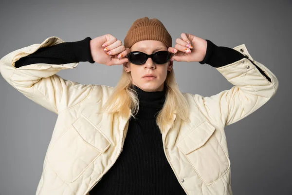 Good looking stylish non binary model in with beanie hat touching sunglasses and looking at camera — Stock Photo