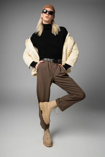 Atraente jovem pessoa não binária em roupa de inverno elegante posando em fundo cinza, moda — Fotografia de Stock