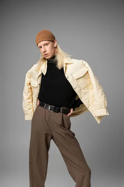 Appealing handsome androgynous person in beanie hat and winter jacket posing on gray backdrop — Stock Photo