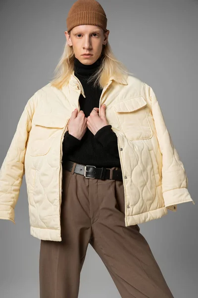 Pessoa andrógina atraente em trajes de inverno na moda posando em fundo cinza com as mãos no colarinho — Fotografia de Stock