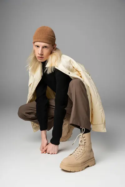 Young androgynous model in winter attire with beanie hat squatting and looking at camera, fashion — Stock Photo
