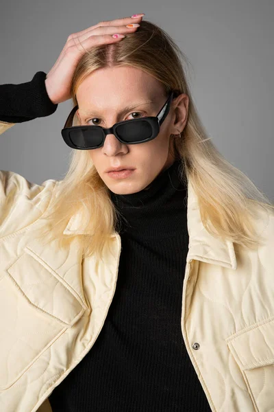 Good looking non binary person with long hair and sunglasses on gray backdrop with hand on head — Stock Photo