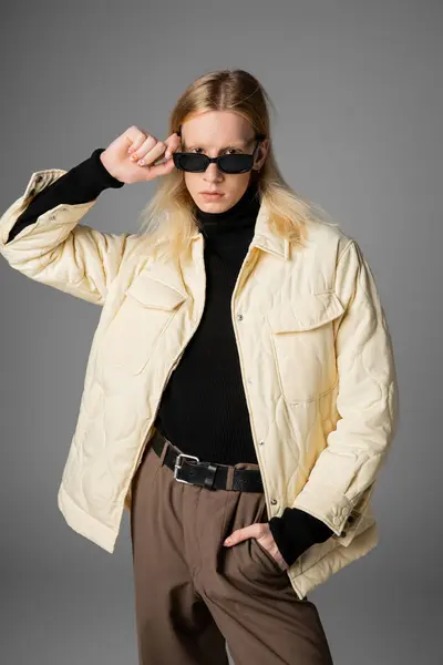 Tiro vertical de jovem andrógino na jaqueta elegante quente tocando óculos olhando para a câmera — Fotografia de Stock