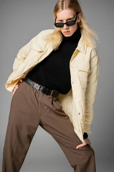 Attraente giovane modello non binario in giacca elegante con occhiali da sole e capelli lunghi guardando la fotocamera — Foto stock