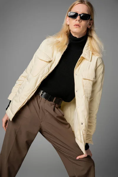 Vertical shot of androgynous model in warm outfit with sunglasses posing on gray background, fashion — Stock Photo
