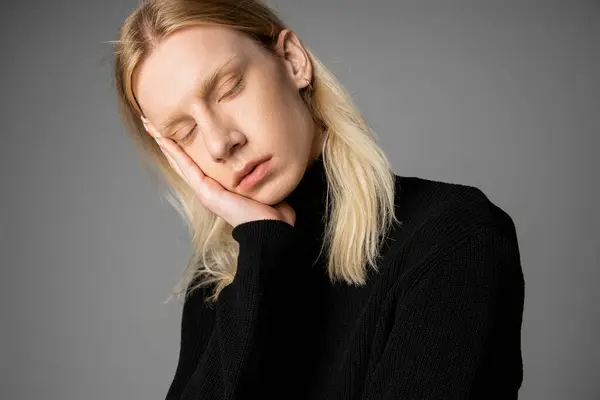 Bonito não binário pessoa em preto gola alta posando com olhos fechados com mão no rosto, moda — Fotografia de Stock