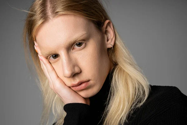 Retrato de jovem não binário pessoa em elegante gola alta preta com a mão no rosto olhando para a câmera — Fotografia de Stock