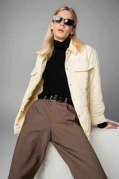 Vertical shot of young handsome non binary person in stylish attire posing on cube, fashion concept — Stock Photo