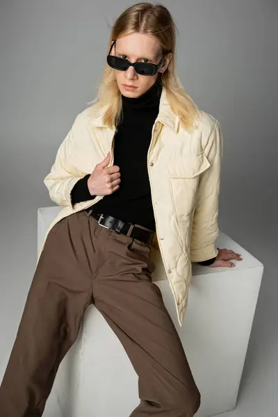 Вертикальный снимок молодой недвоичной модели в зимней куртке и стильных солнцезащитных очках, смотрящих в камеру — стоковое фото