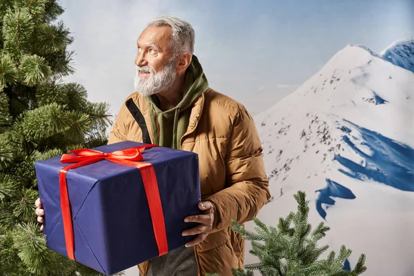 Fröhlicher Mann in warmer sportlicher Jacke mit Geschenk in der Nähe von Kiefer, Winterkonzept — Stockfoto