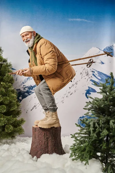 Santa com barba branca agachada no toco da árvore com bastões de esqui sorrindo para a câmera, conceito de inverno — Fotografia de Stock