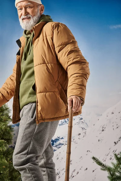 Guapo Santa con barba blanca mirando alegremente a la cámara posando con bastones de esquí, concepto de invierno - foto de stock