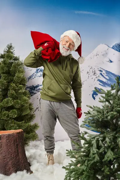Athletic Santa in warm christmassy hat and mittens holding red huge present bag, winter concept — Stock Photo