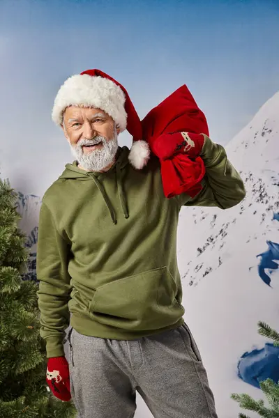Hombre atlético posando con sombrero de Santa y bolsa de Navidad con telón de fondo de montaña, concepto de invierno - foto de stock